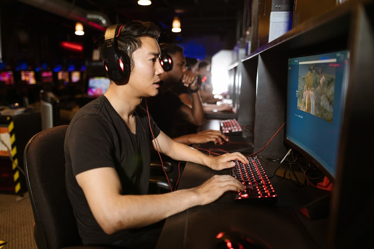 Group of men gaming in an internet cafe, focused on computers.