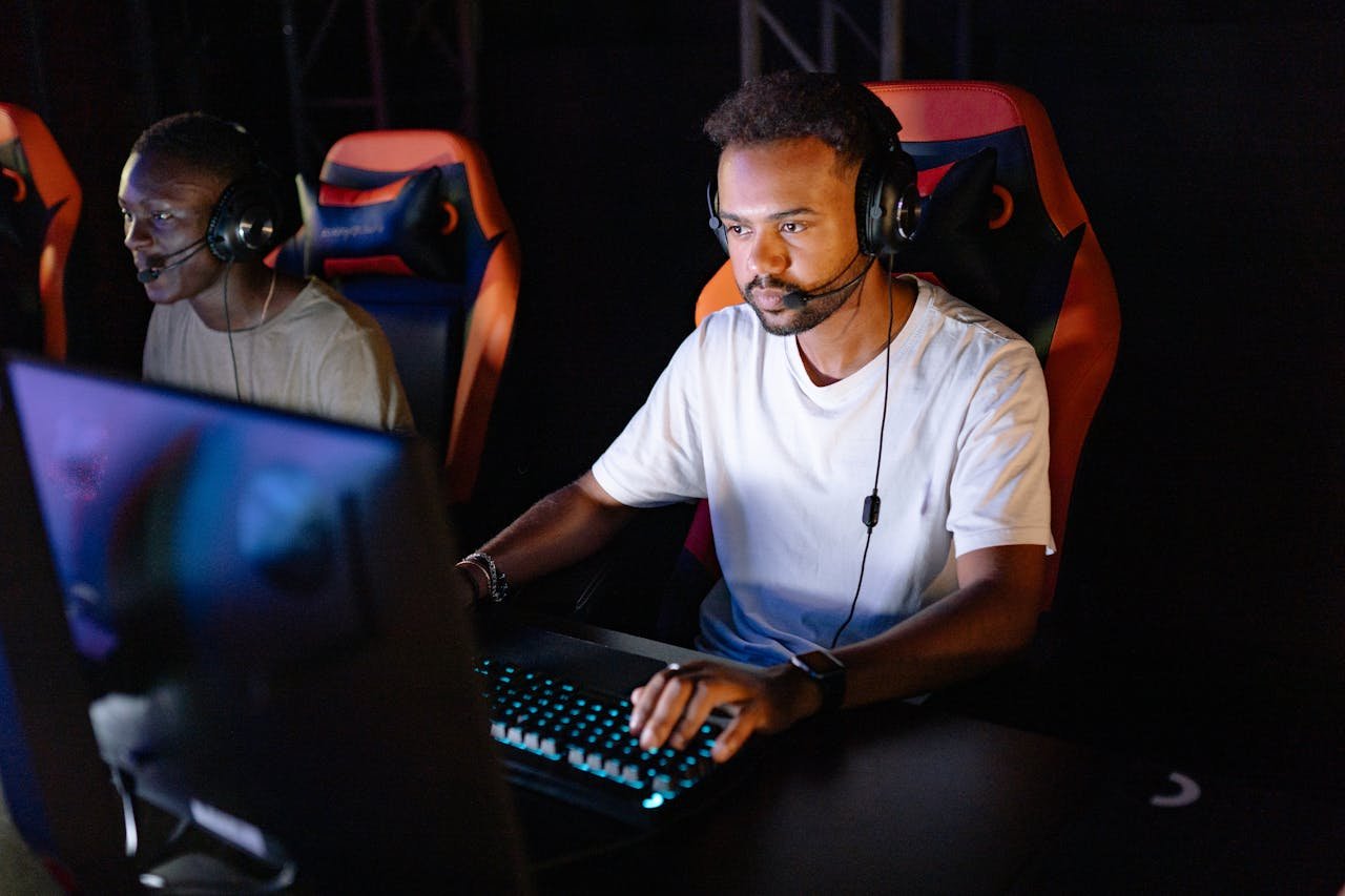 Two young men engaged in an intense esports gaming session with headsets in a dark room.